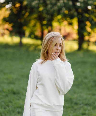 Young blonde girl is wearing a white hoodie smiling and walking in the woods